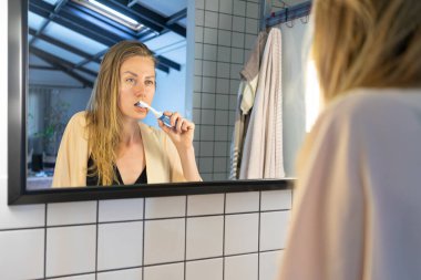 Banyo aynasına bakıp diş fırçasıyla dişlerini fırçalayan güzel bir genç kadın.