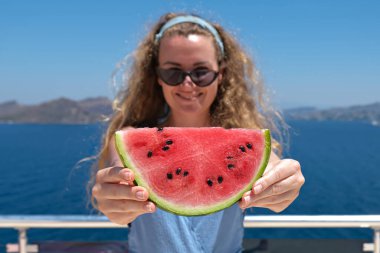 Arka planda deniz manzaralı mayo giymiş bir karpuz dilimiyle gülümseyen güzel bir kadın. yaz tatili