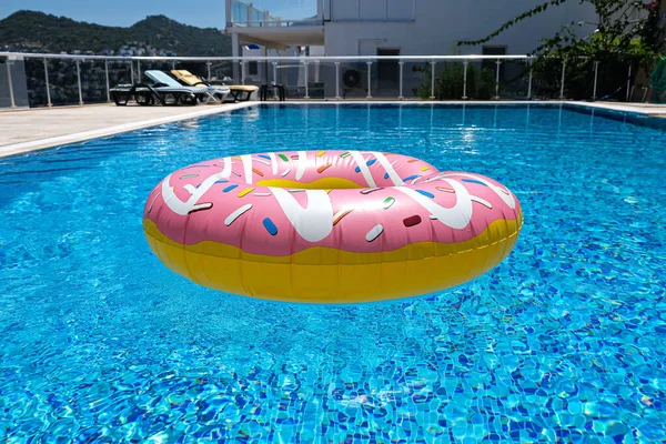 Yüzme havuzunda yüzen pembe şişirilebilir donut donutu. Plaj havuzu aksesuarları. Yaz tatili kavramı
