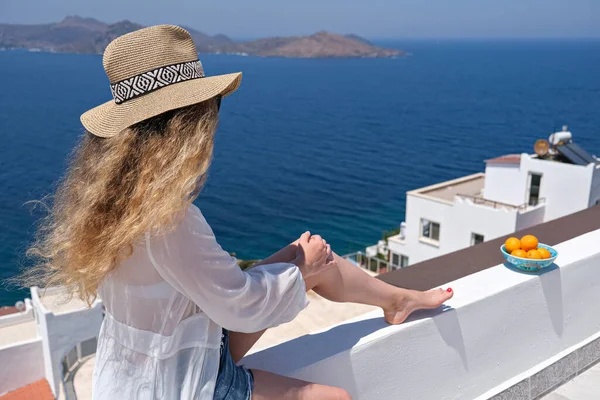 Hermosa mujer joven en vestido blanco sombrero de paja en balcón terraza blanca de la casa o el hotel con vista al mar —  Fotos de Stock