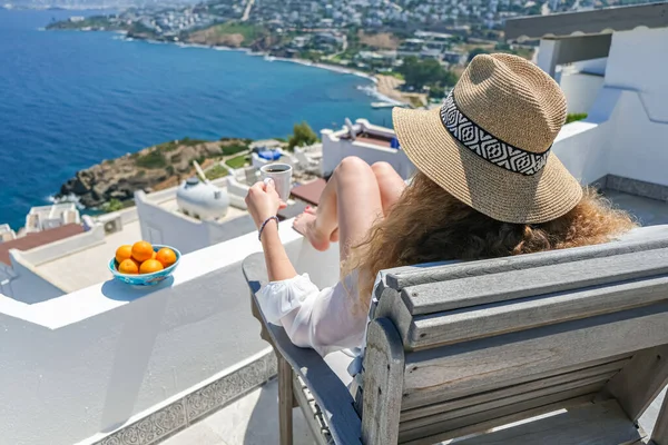 美丽的年轻女子 身穿白衣 头戴草帽 头戴咖啡杯 坐在有海景的房子或酒店的白色阳台上 — 图库照片