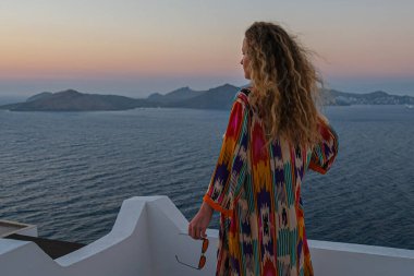 Balkon terasında bir kadın güzel, renkli gün batımını ve deniz manzarasını izliyor..