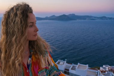 Kadının yüzünü kapayın ve lüks tatil köşkünün terasından gün batımına ve deniz manzarasına bakın..