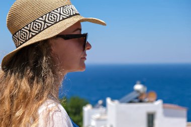 Beyaz gözlüklü, bikinili, hasır şapkalı, tatil köyündeki deniz manzaralı güzel bir kadın..