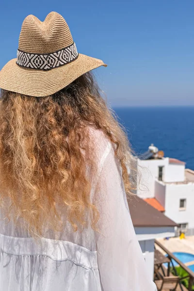 有海景的房子或酒店的白色露台阳台上 戴着白衣草帽的年轻貌美女子 — 图库照片