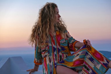 Arka planda deniz ve gün batımı olan renkli elbiseli güzel bir kadın. Tatil köyü Yaz tatili konsepti