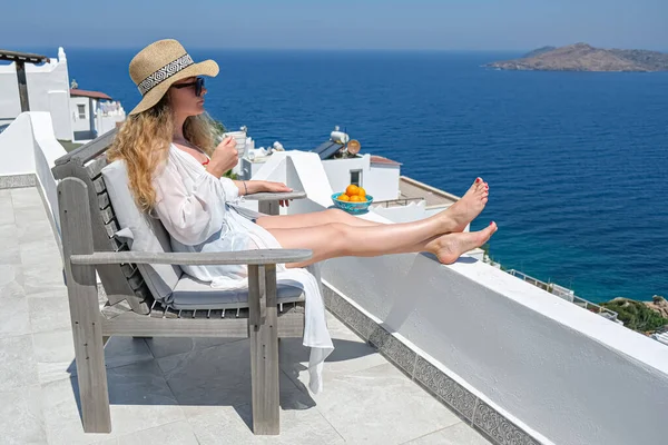 Bella giovane donna cappello di paglia e tazza di caffè seduta sulla terrazza bianca balcone di casa o hotel con vista mare — Foto Stock