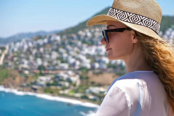 Beyaz gözlüklü, bikinili, hasır şapkalı, tatil köyündeki deniz manzaralı güzel bir kadın.