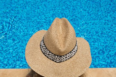 Hasır şapkalı kadın yüzme havuzunun kenarında güneşleniyor..