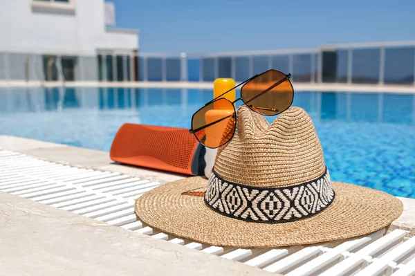 orange coloured beach accessories near swimming pool. Sun cream, sunglasses, music speaker and straw hat.