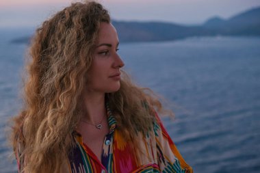 Günbatımını ve lüks tatil köşkünün terasından deniz manzarasını izleyen kadının arkasını kapatın..