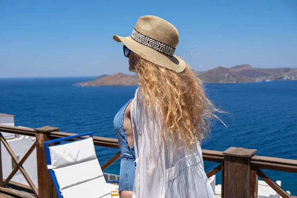 Beyaz mayo ve hasır şapkalı güzel bir kadın. Beyaz teras balkonunda. Deniz manzaralı bir otel ya da ev..