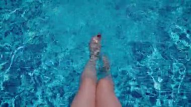 Sıcak bir yaz gününde yüzme havuzunda kadın bacakları ayaklarıyla su sıçratıyor. 4K