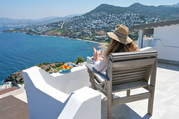 美丽的年轻女子草帽和咖啡杯坐在有海景的房子或酒店的白色阳台上 — 图库照片