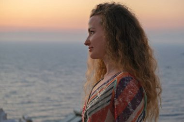 Kadın gün batımına ve lüks tatil köşkünün terasından deniz manzarasına bakıyor.