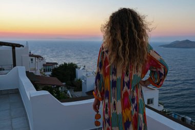 Balkon terasındaki kadın güzel, renkli günbatımına ve denize bakıyor..