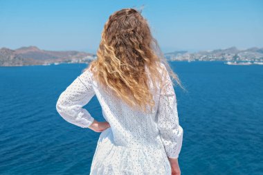 Beyaz elbiseli, güneş gözlüklü güzel bir kadın villa otelinin beyaz terasında Sea View 'a bakıyor.