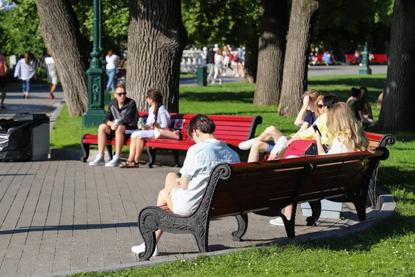 İnsanlar güneşli bir yaz gününde bir bankta oturuyorlar, Aleksanrovsky Garden, Moskova. Arka plan bulanık odak. Rusya Moskova Haziran 2020.