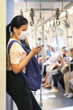 Metro vagonu tıbbi maskeli bir kadın telefona bakıyor. Tayland Bangkok Mart 2020