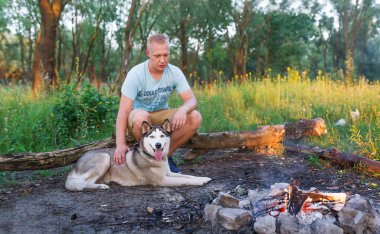 Husky köpek yaz ormanda kamp ateşi hazırlayan adam. Açık havada ormanda hipster treveler. Yatay dikey