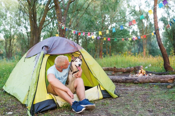 Man embracing husky dog in tent outdoors. Concept of friendship of the man and dog.