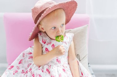 Büyük şapkalı güzel küçük kız kanepede oturan lolipop berbat. Portre portre