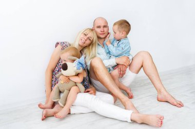 Beyaz aile beyaz arka plan üzerinde oturuyor. Anne, Baba, kızı ile yumuşak oyuncak ve katta oturan oğulları.