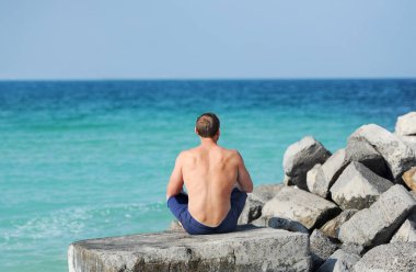 Adam denize bakarak onu geri ile bir taş üzerine oturan çıplak bir gövde ile.