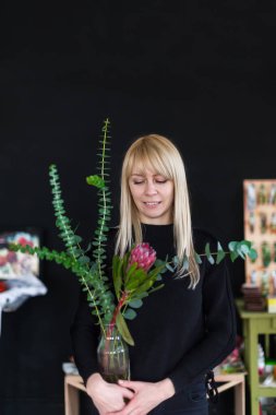 Sarı uzun saçlı Sevimli romantik kadın kırmızı siyah arka plan üzerine protea tutar. Çiçekçi dükkanı ve bitki tasarım ana sınıfı konsepti.