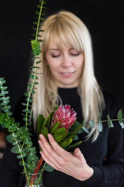 Sarı uzun saçlı Sevimli romantik kadın kırmızı siyah arka plan üzerine protea tutar. Portre portre. Protea seçici odak.