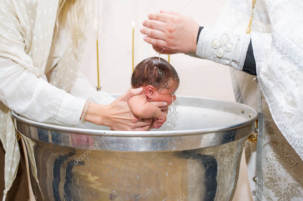 Mother holds child while priest baptizes with holy water. Closeup photo