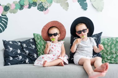 Mutlu mutlu çocukluk kavramını evde kanepede oturan çocuk siyah gözlük ve hasır şapkalar lezzetli lolipop, yemek