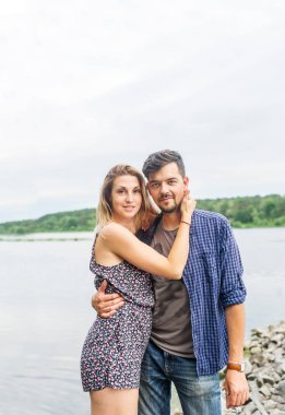 Göl kenarında sarılma genç romantik çift. Mutlu genç adam ve yaz günü itibariyle uzun saçlı güzel kadın portresi. Yatay dikey