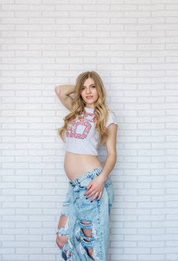 Güzel genç hamile kadın kotun içinde tuğla duvar arka plan üzerinde beyaz bir t-shirt giymiş. Dikey portre