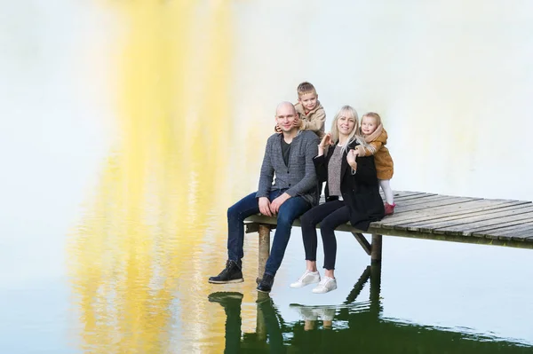 Happy family of four sit on the wooden pier in warm autumn day. Fall family portrait