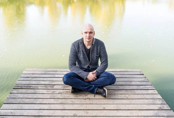 Glatzköpfiger Junger Mann Jeans Sitzt Lotus Pose Auf Dem Holzsteg — Stockfoto