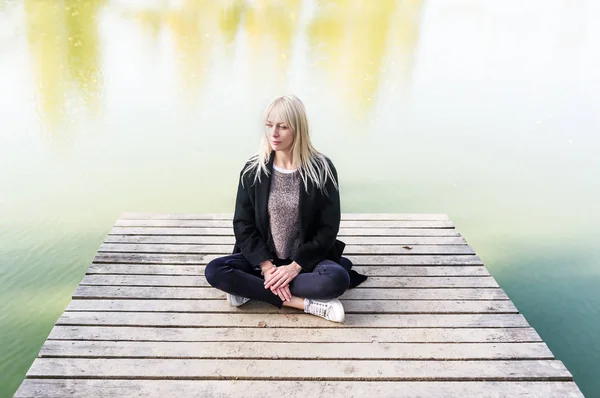 Blondynka Młoda Kobieta Czarnym Płaszczu Siedząc Molo Parku Medytacji Portret — Zdjęcie stockowe