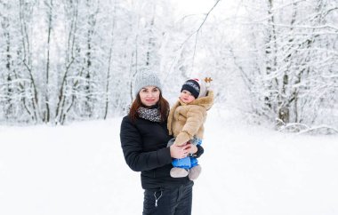 Genç bir anne kucağında bebek oğlunu tutar. Kış Orman yürüyüşleri. Anne ve bebek oğlu olduğunu kış parkta.