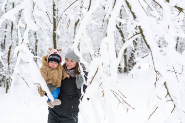 Genç bir anne kucağında bebek oğlunu tutar. Kış Orman yürüyüşleri. Orman karla kaplı. Ağaçlar karda.