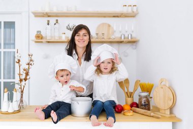 İki küçük aşçılar sittting annesi ile mutfakta masada. Yetişkin meslek çocuk oyunları. Fotoğraf İç.