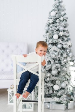 Komik bebek çocuk Noel ağacı arka plan üzerinde beyaz sandalyede oturuyor. Dikey portre