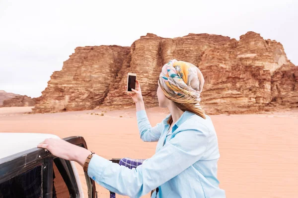 Woman tourist shoots video or photo on mobile phone of the Jordanian desert. Traveler concept. Back view