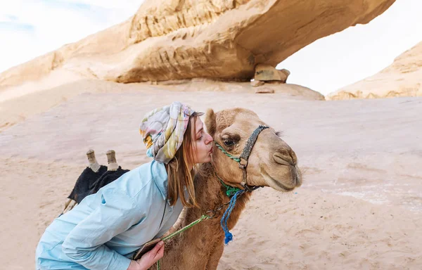 The woman touches with lips a muzzle of a camel in the Jordanian desert. Concept of tourism and travel