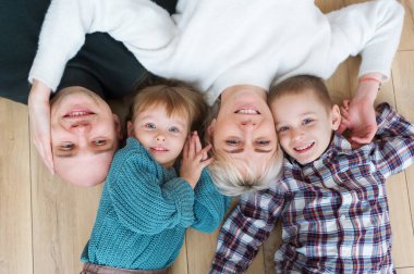 Güzel anne, onların şirin küçük kızı ve kameraya bakıyor ve gülümsüyor, ahşap yerde yatarken oğlu üstten görünüm.