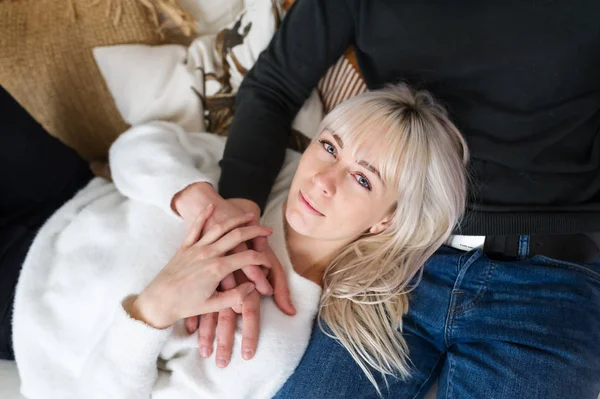 Top view of a cute blonde woman lying on her boyfriend lap on a couch at home. Horizontal portrait