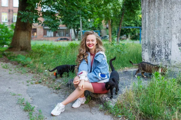 Girl playing in the grass with three cats, enjoying beautiful summer day in city yard