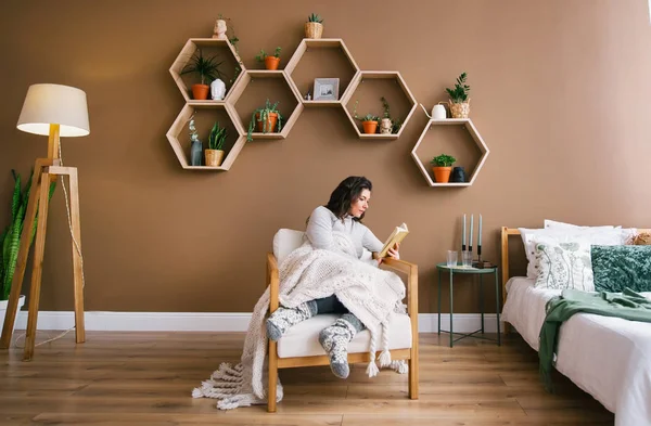 Sevimli kadın daire koltukta oturan bir kitap okuma keyfi