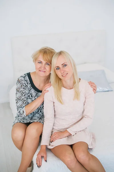 Dos hermosas mujeres una madre y su hija sentadas en la cama en la habitación blanca —  Fotos de Stock