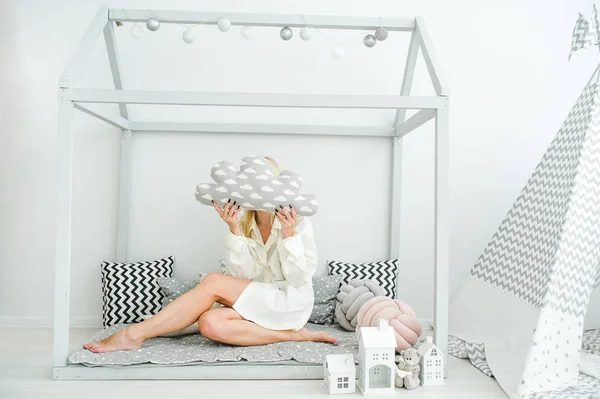 Een mooi blond meisje verborg een gezicht achter een wolk van speelgoed en zitten op een verdieping in de kinderkamer — Stockfoto