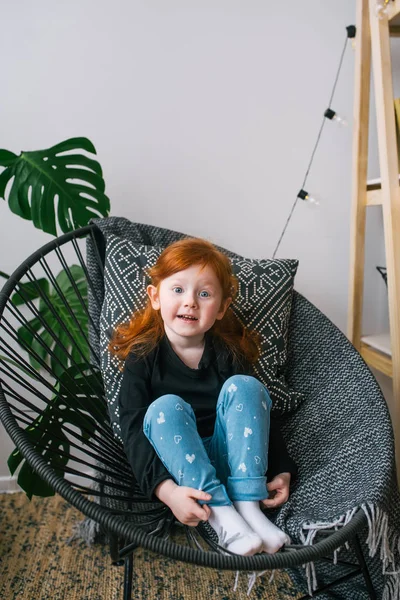 Pequena menina ruiva bonito em jeans sentar na poltrona. Emoções surpresas — Fotografia de Stock